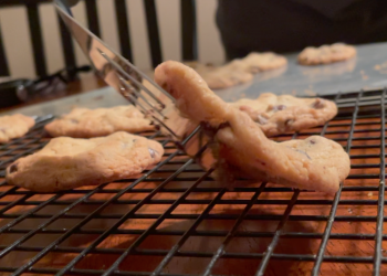 Image of cookies being put on a cooling crack my a metal spatula.